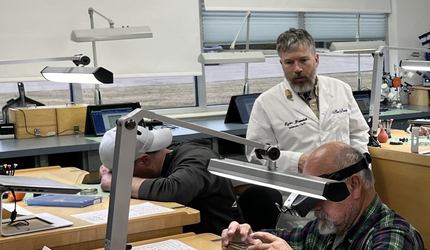 Ryan Bramlett assisting students at watchmaking benches in a classroom at AWCI headquarters